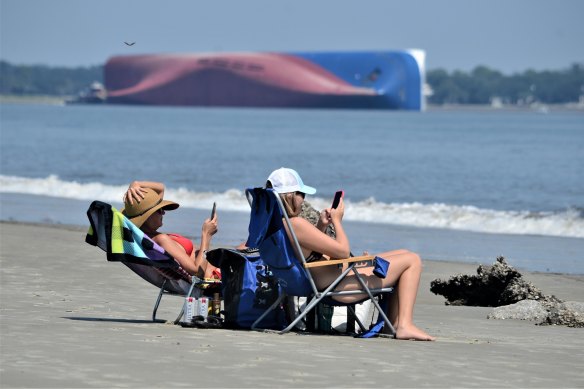 Beachgoers relax on Jekyll Island's Driftwood Beach as the Golden Ray cargo ship is capsized in the background.