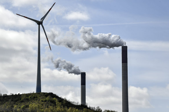 Chimneys of a coal-fired power plant smoke beside a wind turbine in Gelsenkirchen, Germany.