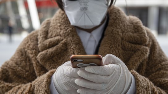 A pedestrian, wearing a fast mask and gloves, checks her phone in Milan, Italy.