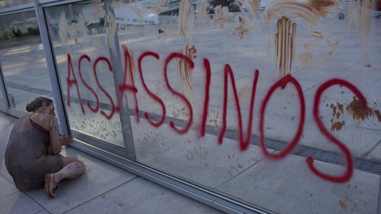 A woman covered in mud, kneels next to the word "Assassins", during a protest outside the Rio de Janiero office Brazilian mining company Vale last month.