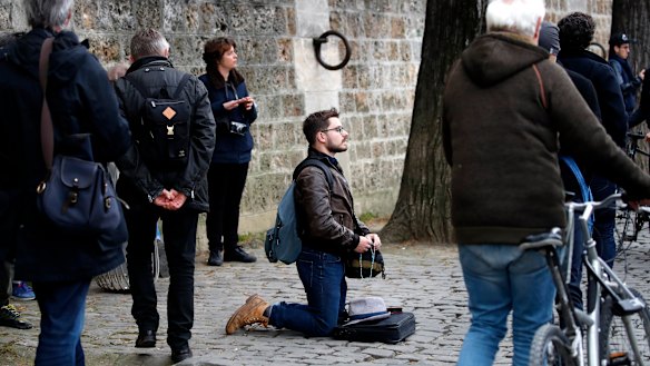 A man kneels as people watch and photograph the Notre Dame cathedral after the fire in Paris.