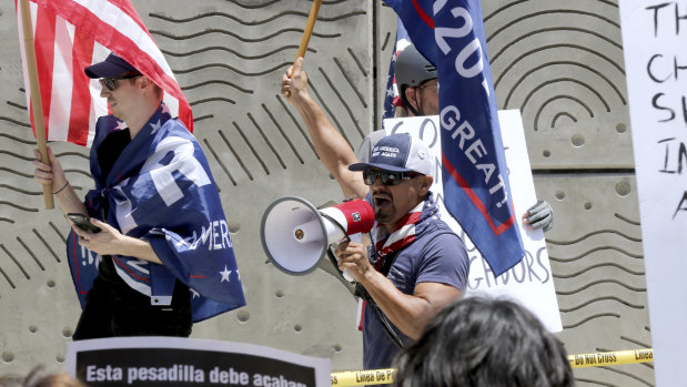 Three Trump supporters hold flags and yell at people while being kept apart by the LAPD at the 'Families Belong Together: Freedom for Immigrants' march on Saturday.
