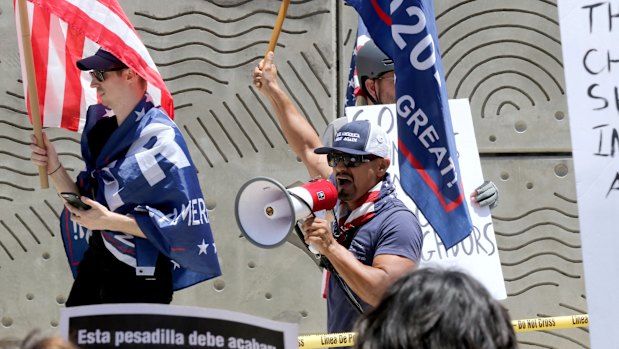 Three Trump supporters hold flags and yell at people while being kept apart by the LAPD at the 'Families Belong Together: Freedom for Immigrants' march on Saturday.