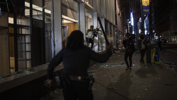 New York police run towards people as they jump out of a store with items they took hours after a solidarity rally.
