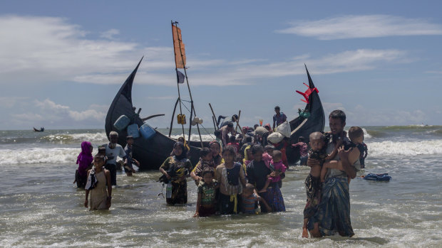 A Rohingya man carries two children to shore in Shah Porir Dwip, Bangladesh, after they arrived on a boat from Myanmar last year.