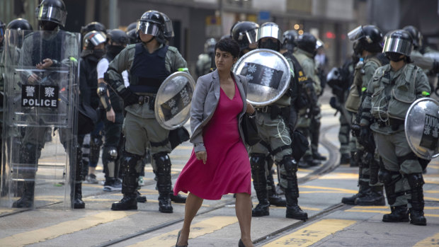 A woman walks past Hong Kong riot police clearing up a road in the Central district of Hong Kong on Friday.