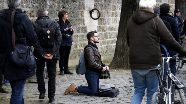 A man kneels as people watch and photograph the Notre Dame cathedral after the fire in Paris.