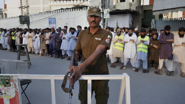 A Pakistani police officer stands guard while people offer funeral prayers  in Lahore for the victims of a Friday suicide bombing in Mastung district that killed 128 people on Sunday, July 15.
