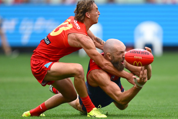 Max Gawn of the Demons handballs whilst being tackled by Sam Clohesy of the Suns.
