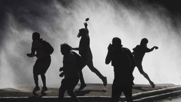 Anti-government demonstrators throw rocks at a police water canon trying to disperse them in Santiago, Chile, on Friday.