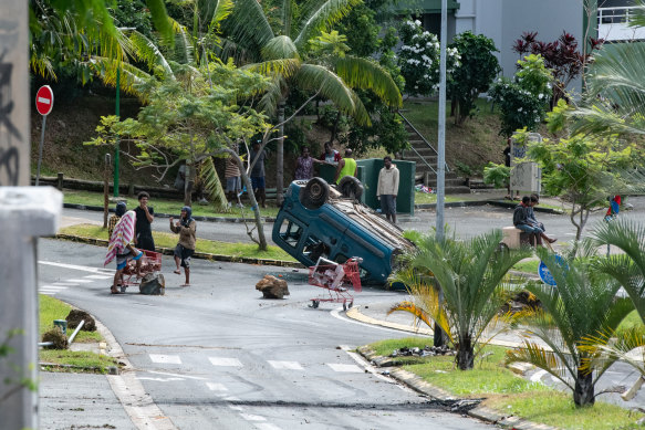 People gather near an overturned car in the Motor Pool district on Tuband in Noumea.