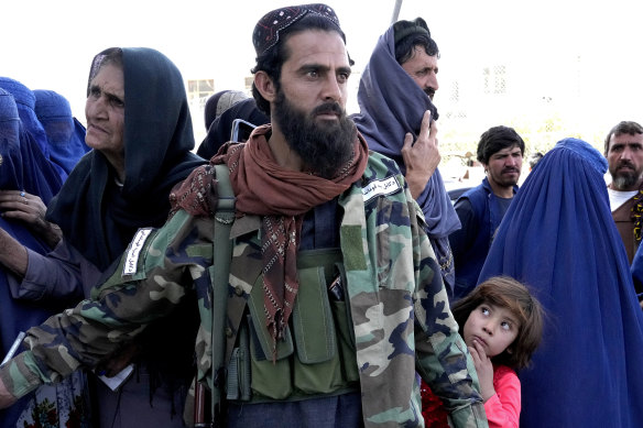 A Taliban fighter stands guard as people receive food rations distributed by a Saudi humanitarian aid group, in Kabul, Afghanistan. The country has been plunged into a humanitarian crisis since the Taliban took over.
