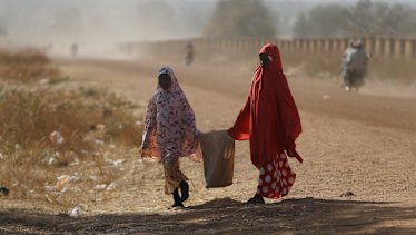Two women walk past the Government Science Secondary School in Kankara on Tuesday.