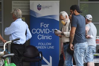 People wearing face masks walk past the sign for the COVID-19 Clinic at St Vincent’s Hospital in Darlinghurst, Sydney.