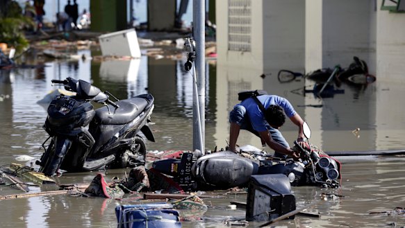 An Indonesian man tries to get his motorbike upright at a tsunami devastated area in Talise beach, Palu.