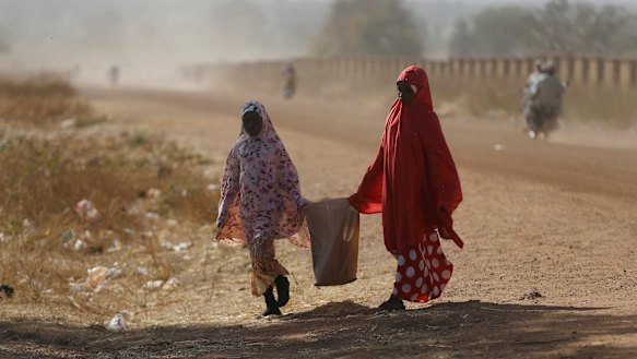 Two women walk past the Government Science Secondary School in Kankara on Tuesday.