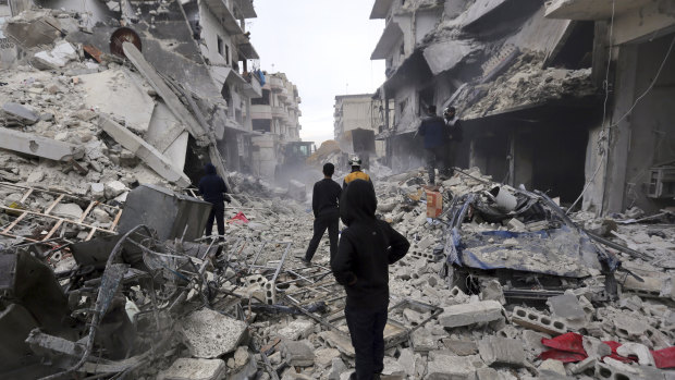 Syrian rescuers use a bulldozer to remove rubble of a destroyed building that covers a street after airstrikes in the town of Ariha, in Idlib province, Syria.