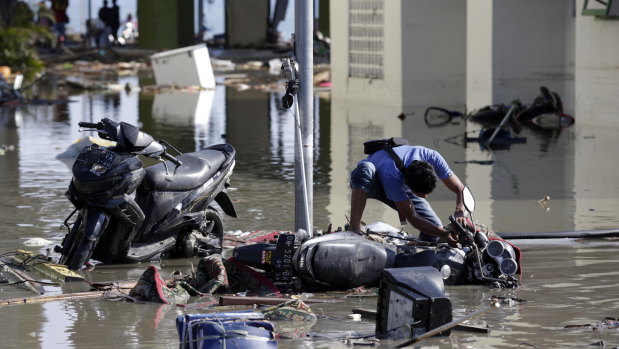 An Indonesian man tries to get his motorbike upright at a tsunami devastated area in Talise beach, Palu.