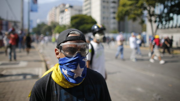 An anti-government protester, masked with a Venezuelan flag, looks toward security forces during clashes near La Carlota airbase in Caracas, Venezuela. 