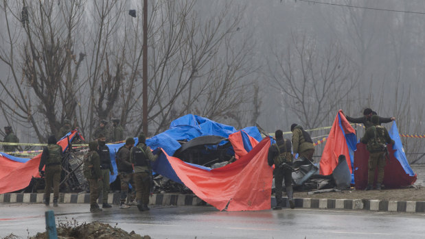 Indian policemen cover the wreckage of a bus with plastic sheets at the site of the explosion in Pampore, Indian-controlled Kashmir on February 15.