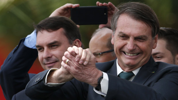 Accompanied by his son Senator Flavio Bolsonaro, left, Brazilian President Jair Bolsonaro flashes a victory clasp at the launch of his new political party, Alliance for Brazil, in Brasilia.