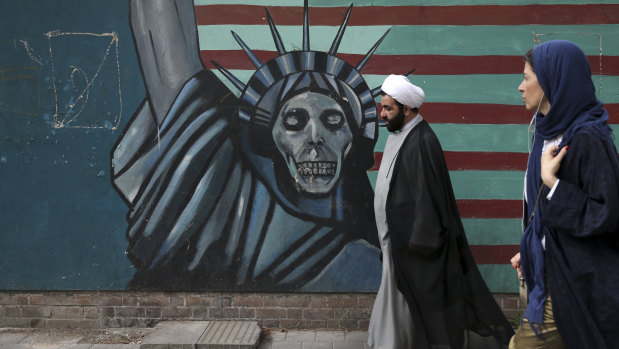 A cleric and a woman walk past an anti-US mural painted on the wall of the former American Embassy in Tehran.