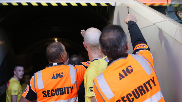 Umpire Matthew Nicholls and security guards point out the Carlton fan. 