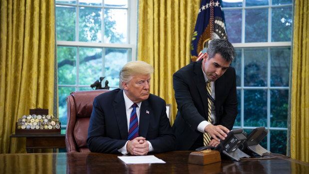 A White House aide assists US President Donald Trump connect a phone call in the Oval Office.