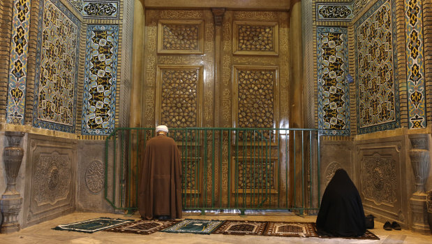 A cleric and a woman pray behind a closed door of the Fatima Masumeh shrine in Qom, Iran.