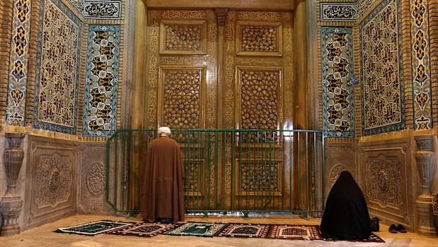 A cleric and a woman pray behind a closed door of the Fatima Masumeh shrine in Qom, Iran.