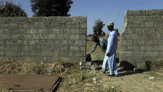 People inspect a wall and metal door broken by the gunmen who kidnapped Government Science Secondary School students in Kankara.