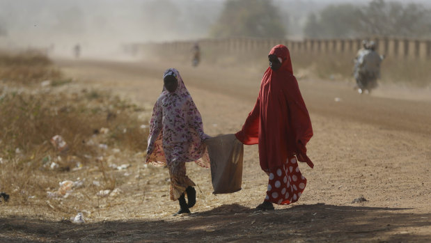 Two women walk past the Government Science Secondary School in Kankara on Tuesday.