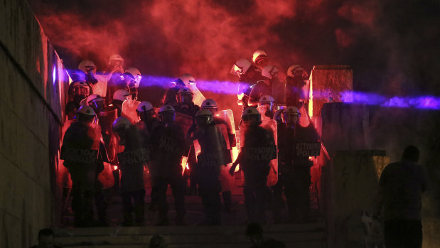 A flare thrown by protesters highlights riot police guarding the parliament during a demonstration against the agreement between Greece and Macedonia over a dispute of the former Yugoslav\'s republic name, in Athens, on Saturday.