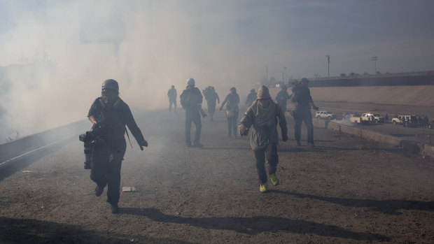 Migrants and journalists run from tear gas launched by US agents at the Mexico-US border.