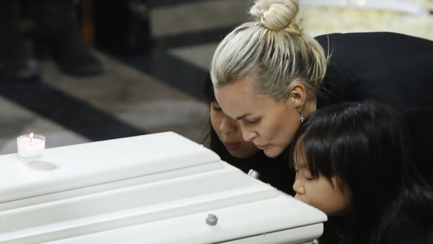 The widow of French rocker Johnny Hallyday, Laeticia Hallyday, and her children, Jade, left, and Joy, kiss Johnny Hallyday's coffin at his 2017 funeral. 