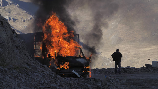 A man stands near his burning car which caught on fire during the climb along the road to a mountain pass, near the border between Nagorno-Karabakh and Armenia.