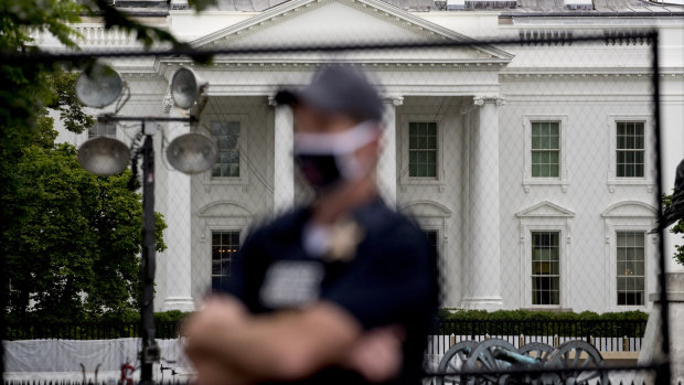 A uniformed Secret Service agent stands on the street in front of the White House.