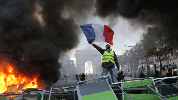 A demonstrator waves the French flag on a burning barricade on the Champs-Elysees