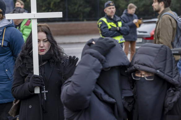 A woman holds up a cross next two Muslim girls while Rasmus Paludan burns the Koran outside the Turkish embassy in Stockholm.