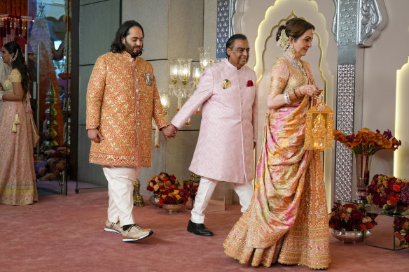 Billionaire Mukesh Ambani, centre, takes his son Anant Ambani by the hand as they walk with Nita Ambani, right, at the wedding.