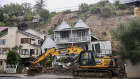 An excavator works at a home badly damaged by flooding and landslides in Auckland.