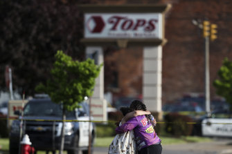 Люди обнимаются за кадром после стрельбы в супермаркете в субботу, 14 мая 2022 года, в Буффало, штат Нью-Йорк.