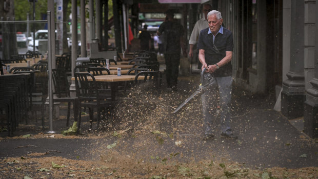 University Cafe owner Giancarlo Capriol cleaning up his shop front on Lygon Street after the storm. 