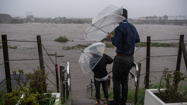 People look at the flooded Tama River during Typhoon Hagibis on October 12.
