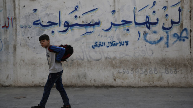 A Syrian student walks next a wall with Arabic that reads: "We will not emigrate we will confront, no to the Turkish occupation," in Manbij, north Syria. On  December 28, 2018, Syria's military said it entered the flashpoint Kurdish-held town of Manbij, where Turkey has threatened an offensive. a claim that was refuted by US  troops who patrol the town. The conflicting reports reflect the potential for chaos in the wake of the US surprise decision to withdraw troops from Syria. 