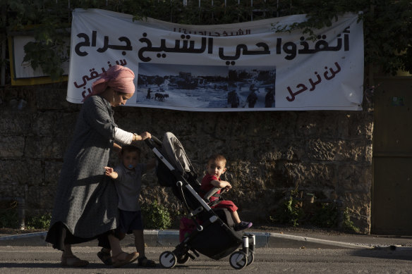 A Jewish settler and her children walk in Sheikh Jarrah. The banner in Arabic reads: “Sheikh Jarrah neighbourhood - we will not leave - we will remain steadfast.”