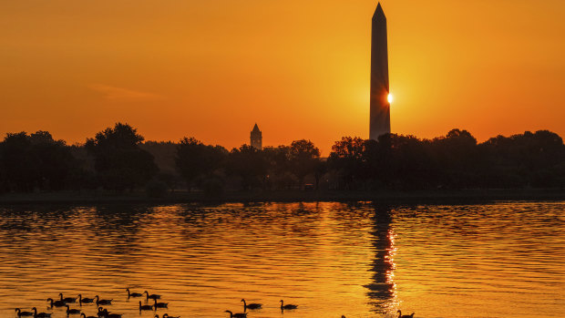 The sun peaks around the Washington Monument as geese float down the Potomac River in Washington as a hot day breaks on Sunday.