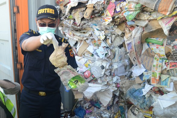 Indonesian Customs official Dhion Priharyanto holds up a used nappy, soft drink containers and a plastic of organic raspberries mixed in with paper that was supposed to be recycled. Instead, it will be sent back to Australia.