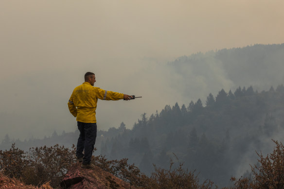A firefighter with the California Office of Emergency Services monitors spot fires on Big Ridge, seen smoldering in the background, during the Walbridge portion of the LNU Lightning Complex fire in Sonoma County, California.