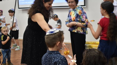 The elders hand out bags of chocolate money to kick-off the dreidel game for the young ones attending the synagogue's "Shabbat + Hanukkah" services.